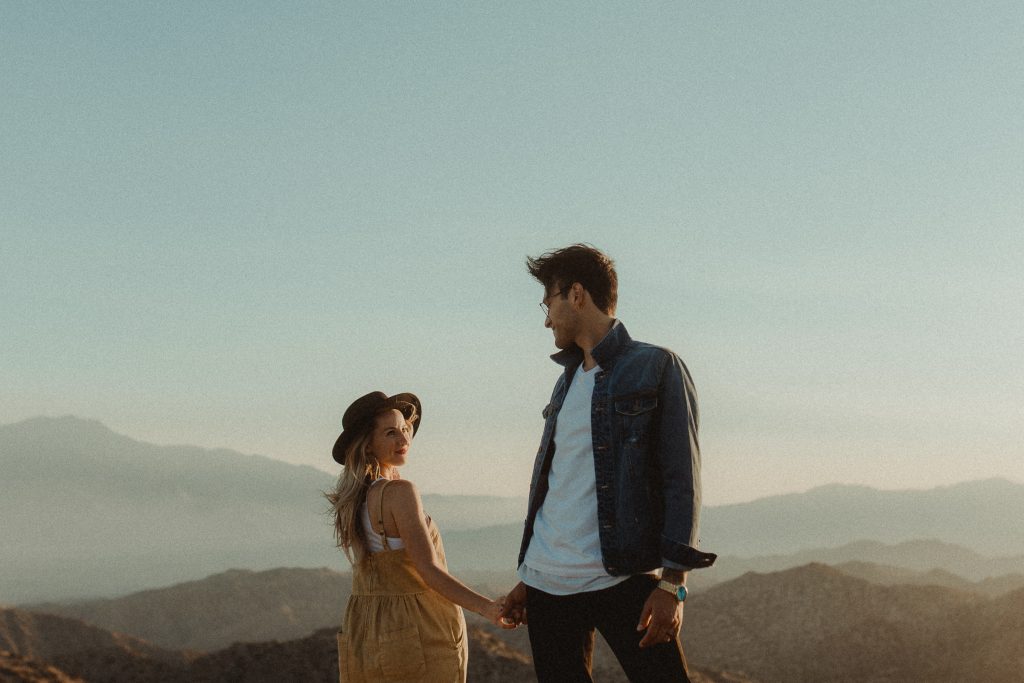 Couple holds hands for their engagement photos during sunset overlooking the valley in Joshua Tree California
