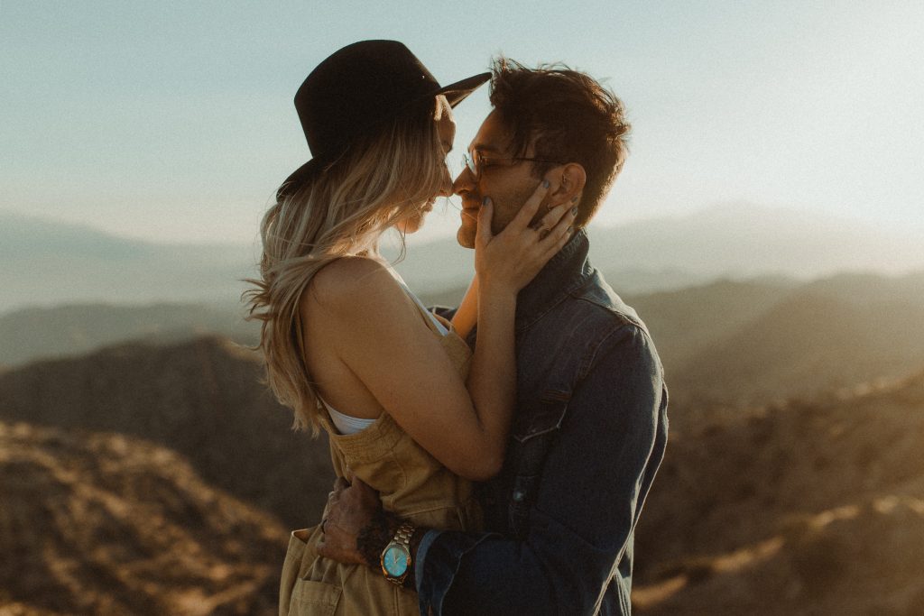 Couple embraces for their engagement photos during sunset overlooking the valley in Joshua Tree California